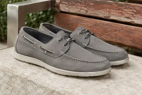 Mocassins bateau gris à lacets élastiques et semelle en caoutchouc posés sur une pierre claire