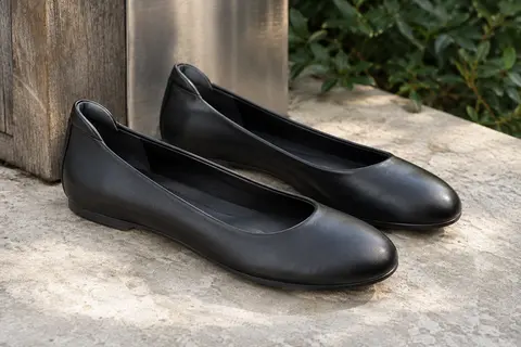 Ballerines noires à bout rond posées sur une pierre claire dans un décor urbain sobre.