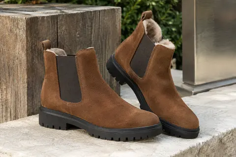 Bottines Chelsea en daim châtaigne avec doublure douce et semelle extérieure crantée, posées sur une pierre claire.